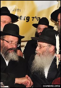 Rabbi Nachman Holtzberg, left, father of slain Chabad-Lubavitch emissary Rabbi Gavriel Holtzberg, shakes the hand of religious scribe Rabbi Moshe Klein after filling in one of the last letters of the Torah scroll destined for his slain son’s reopened Chabad House. (Photo: Boruch Ezagui)