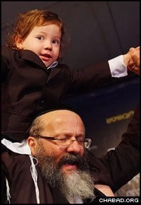 Rabbi Nachman Holtzberg of Brooklyn, N.Y., carries his grandson Moshe on his shoulders for a round of dancing on occasion of the little boy’s third birthday.