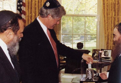 President Bill Clinton places a dollar bill in a charity box after receiving members of the American Friends of Lubavitch in the White House.