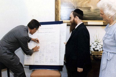 President George H.W. Bush signs the Education Day U.S.A. proclamation, as the First Lady Barbra Bush and Rabbi Abraham Shemtov look on.