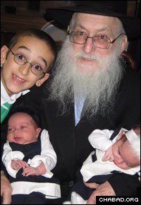 Joined by his grandson, Mendel Serebryanski, Rabbi Pinchus “Pinny” Krinsky holds newborn twin granddaughters Shaina Bracha and Pearl Serebryanski.