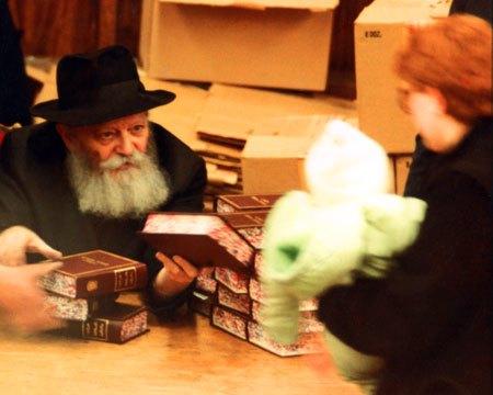 The Rebbe hands a Tanya, the fundamental text of Chabad philosophy, to a small child held in his mother's hands (Photo: Lubavitch Archives).