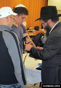 Rabbi Yossy Gordon, executive vice president of the Chabad on Campus International Foundation, helps a student don the prayer boxes known as tefillin.