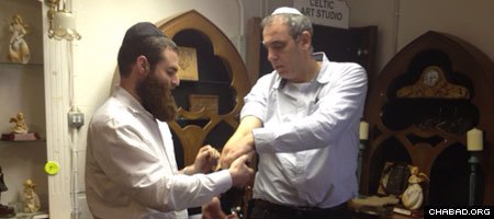 A travelling Chabad-Lubavitch rabbinical student helps a Jewish man don the prayer boxes known as tefillin.