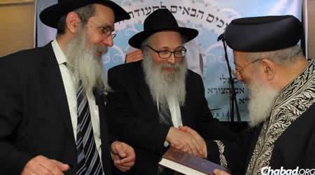 Rabbi Yona Matusof, center, presents Rabbi Shlomo Moshe Amar with a book penned by his father, who was a close friend of Baba Sali, as Rabbi Yosef Posner looks on.