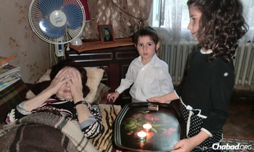 Children in Sumy help an elderly woman light Shabbat candles. (File photo)
