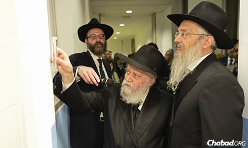 Rabbi Gershon M. Garelik, the first Chabad emissary to Italy who started his shlichus in 1958, affixes a mezuzah in the school, flanked by school director Rabbi Igal Hazan on the left and school dean Rabbi Avraham Hazan on the right.