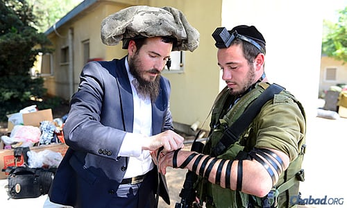 Rabbi Chaim Nochum Cunin, visiting Israel from Chabad West Coast Headquarters in Los Angeles, wrapped tefillin with a soldier earlier this week while temporarily relieving him of his head gear.