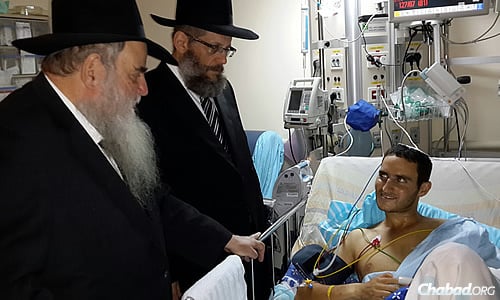 Rabbi Moshe Kotlarsky, left, and Rabbi Yosef Yitzchak Aharonov visit a wounded soldier.