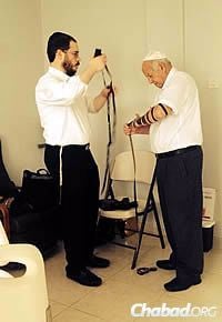 Rabbi Raskin wraps tefillin with Raymond Doweck&#39;s brother, Albert Doweck.