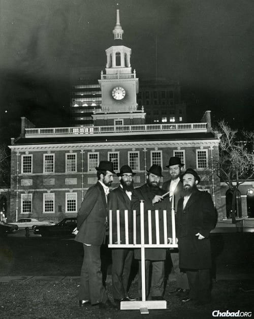 Rabbi Abraham Shemtov, right, in front of Independence Hall in Philadelphia, lighting the very first public menorah in 1974. With him were yeshivah students who helped build the wooden menorah from scratch. (Photo: Lubavitcher Center)