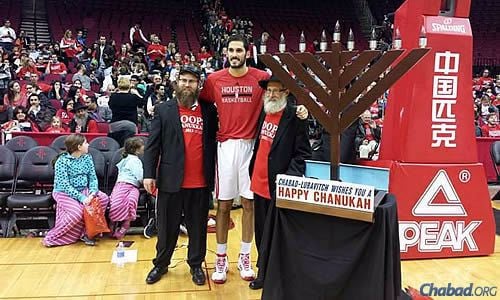 On the Houston Rockets court from a previous year are, from left, Rabbi Mendy Traxler of Chabad Outreach of Houston, Israeli basketball player Omri Caspi and Rabbi Moishe Traxler, director of Chabad Outreach of Houston. “It’s an awesome medium” to celebrate Chanukah, says Rabbi Mendy Traxler.