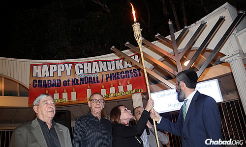Shirley Sotloff takes the torch to light the shamash, the helper candle. Mermelstein is to the right, next to Arthur Sotloff. (Photo: Marta Villalba)