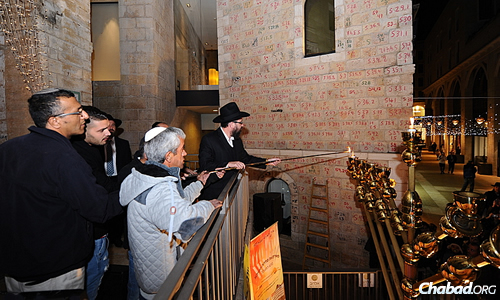 Kutner lights the first candle on the menorah, assisted by family members. (Photo: Mendy Hechtman)