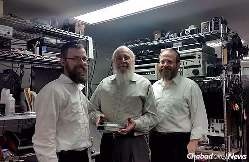 Director of JEM Rabbi Elkanah Shmotkin, left, with Baruch Bongart, holding a tape that was missing for years; next to him is his son Yisroel. After many hours of searching, the VHS tape was finally recovered. (JEM Photo)