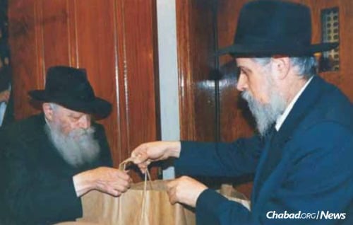 Handing over a bag of gifts and momentos people had given to the Rebbe during Sunday &quot;dollars distribution.&quot;