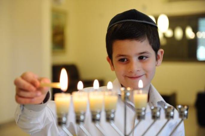 Jewish boy lighting the fourth Hanukkah candle on his Menorah.
