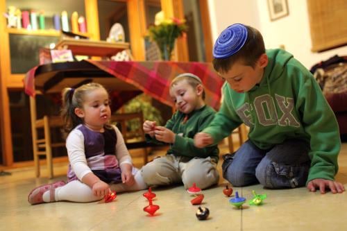 Jewish children playing with the dreidel on the floor.