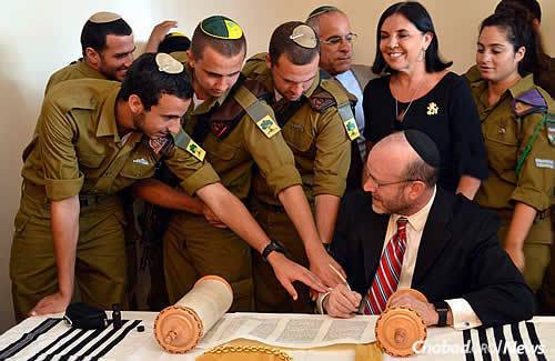 Soldiers reach to assist sofer (scribe) Ronnie Sieger in writing the last letters of the Torah; next to them are Max Steinberg&#39;s parents, Stuart and Evie Steinberg. (Photo: Lone Soldier Center)