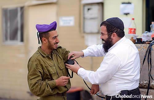 Rabbi Cohen helps a soldier put on tefillin.