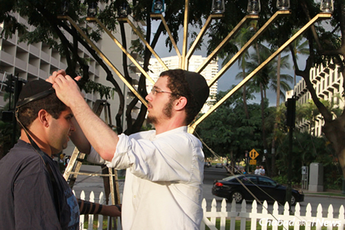 A rabbinical student helps a celebrant don tefillin.