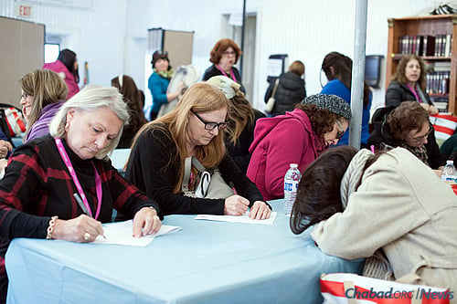 Women writing their notes before entering the Ohel (Photo: Bassie Vorovitch).