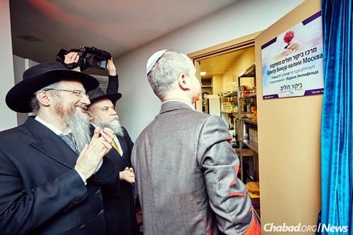 Rabbis Lazar and Barada look on as a supporter reads the sign on a new commercial kitchen inaugurated at Lazar's daughter's sheva brachot ("seven blessings").