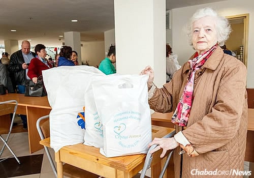 An elderly woman displays bags filled with holiday food and staples. All donations came from the public in response to an extensive ad campaign.