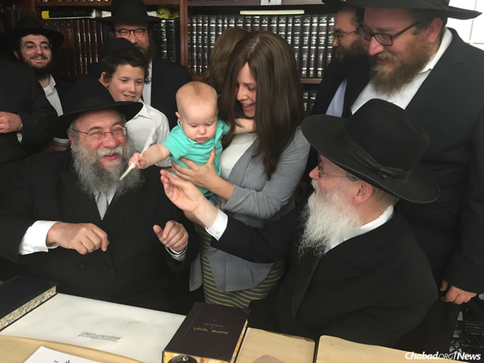 Rivky Berman's youngest nephew, Zalman Backman, gets ready to write a letter in “Rivky’s Torah,” assisted by Rabbi Yisrael Deren, seated at left, and the scribe, Rabbi Moshe Klein, at right.