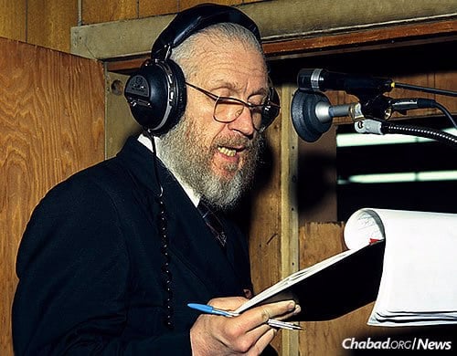 Rabbi JJ Hecht reads from his notes during a live running English translation of the Rebbe’s Yiddish talks at a farbrengen. The translation, later joined by others in Hebrew, French and Russian, was broadcast over shortwave radio. (Photo: JEM/The Living Archive)