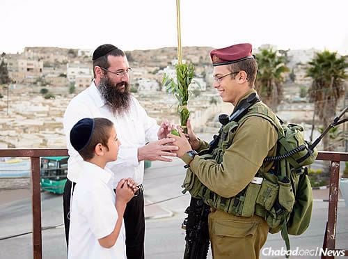Rabbi Danny Cohen of Chabad of Hebron and his son Shneor offer the lulav and etrog to a soldier during Sukkot. (Photo: Israel Bardugo)