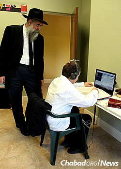 The rabbi looks on as Yehoshua Greenberg studies in the computer library.