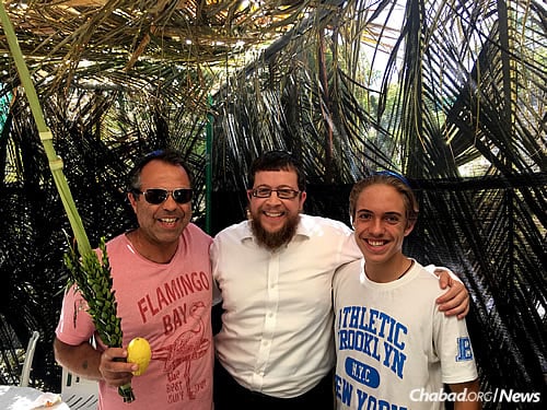 Haim David Helias, left, and his son, Abel, join the rabbi in the sukkah.